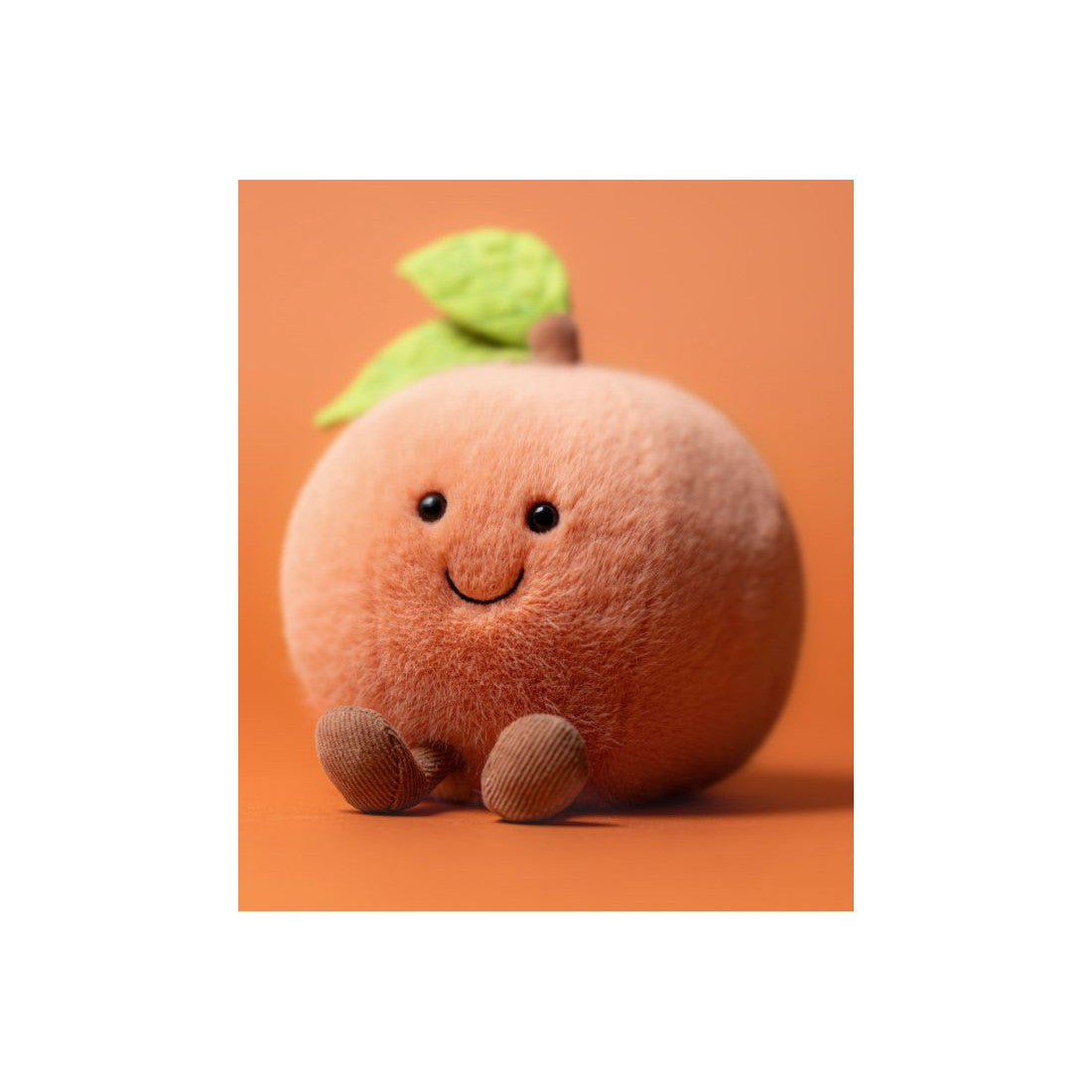 Uśmiechnięta buzia i brązowe nóżki brzoskwini Jellycat na pomarańczowym tle