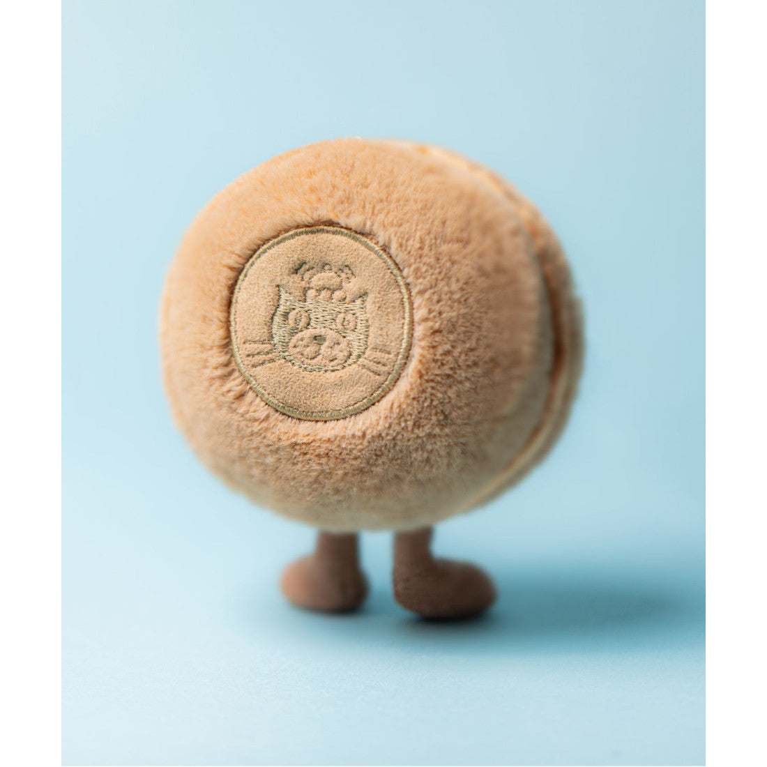 Maskotka Jellycat Amuseables – Makaronik Czekoladowy Mona 12 cm, na nóżkach, widok z tyłu, zdjęcie na błękitnym tle