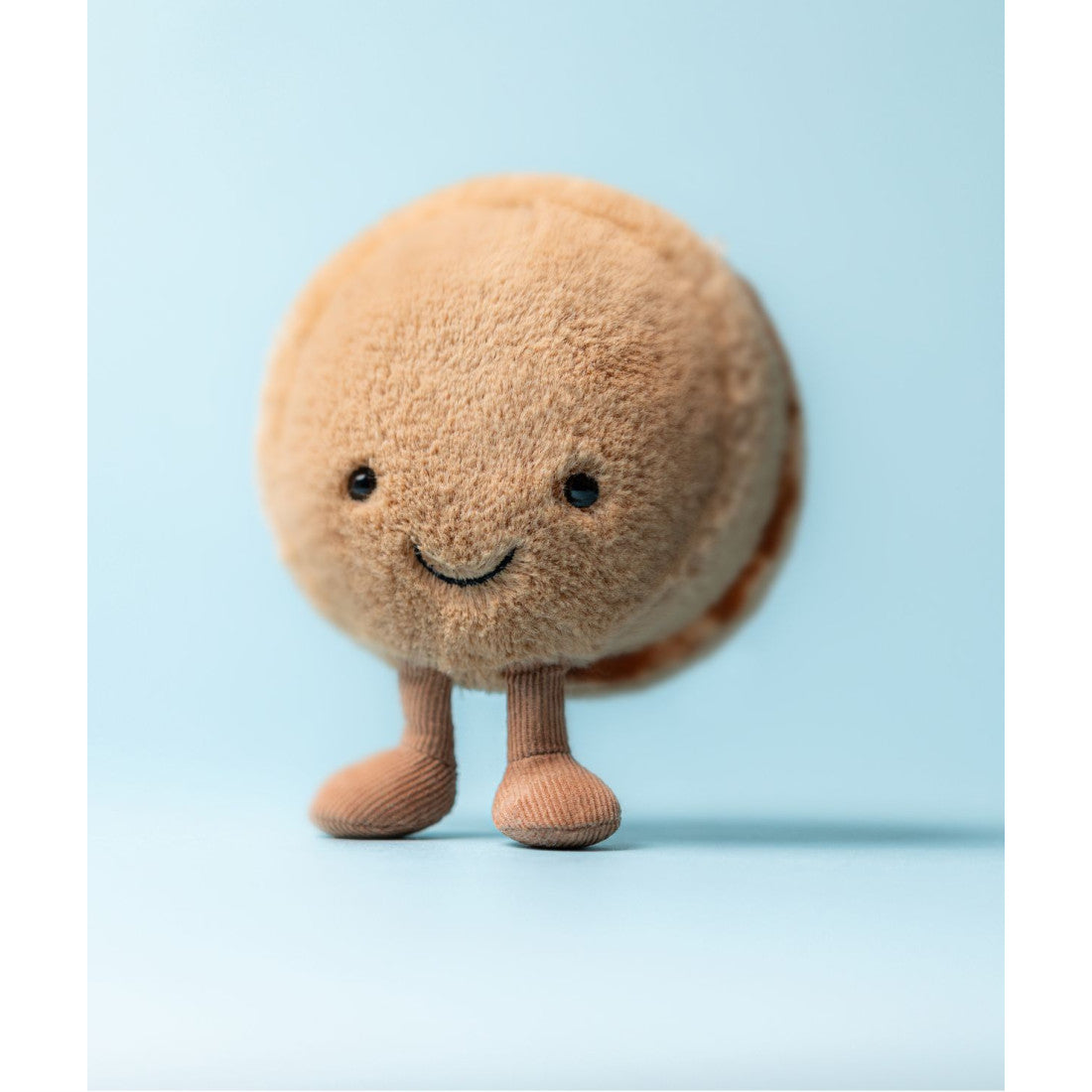 Maskotka Jellycat Amuseables – Makaronik Czekoladowy Mona 12 cm, na nóżkach, zdjęcie na błękitnym tle